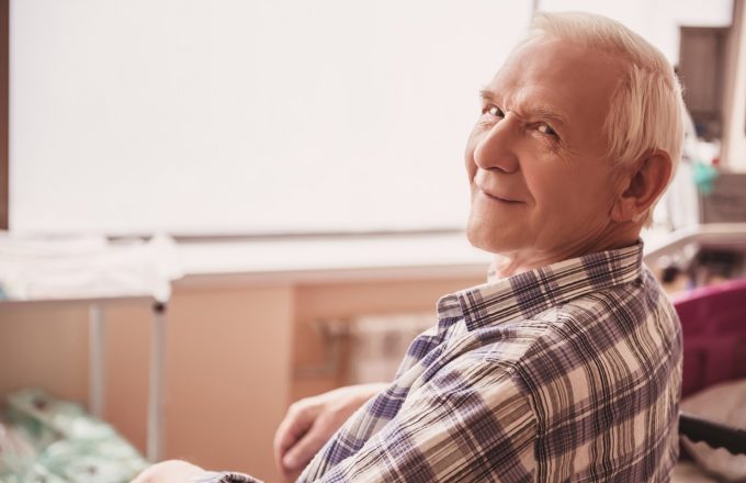 Handsome old man is looking at camera and smiling while sitting in wheelchair in hospital ward