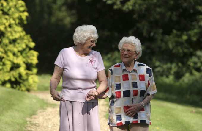 Two older ladies walk arm in arm in a sunlit park