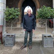 Malcolm standing smiling between two bay trees