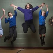 Teacher and children jumping up against a grey wall