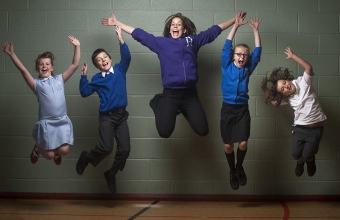 Teacher and children jumping up against a grey wall