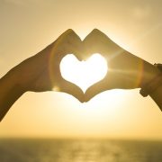 hands making a heart shape with the sun shining through the heart