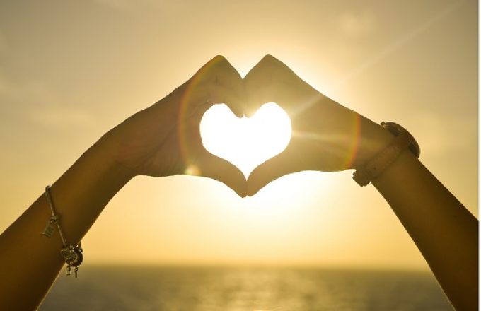 hands making a heart shape with the sun shining through the heart