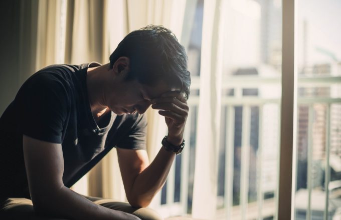 Young person sitting on bed by window, head in hand
