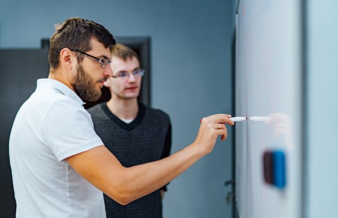 A male tutor and a young male student plan a strategy on a whiteboard