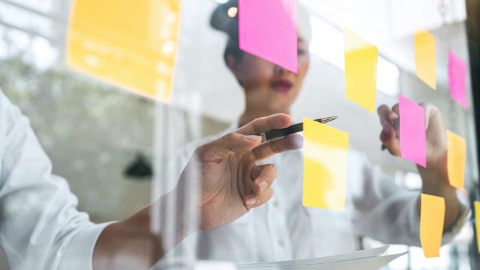 Young people write on a glass wall and use post it notes to plan a strategy