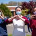 Three nurses standing outside in the sun wearing surgical face masks and holding their hands up in the shape of hearts