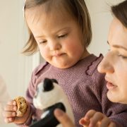 Portrait view of girl with down syndrome holding cookie and looking at her panda toy while standing near her mother.
