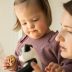 Portrait view of girl with down syndrome holding cookie and looking at her panda toy while standing near her mother.
