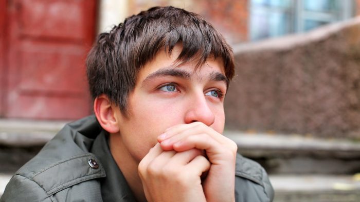 adolescent male sits on steps looking pensive