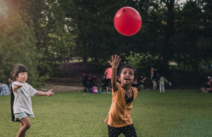 children playing with red balloon in park