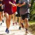 A group of high school runners are training together on a dirt path on a sunny afternoon, running toward the camera.