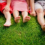 children's legs on the grass. bare legs of little girls sitting on the meadow. Selective focus, children sit on the grass with bare legs