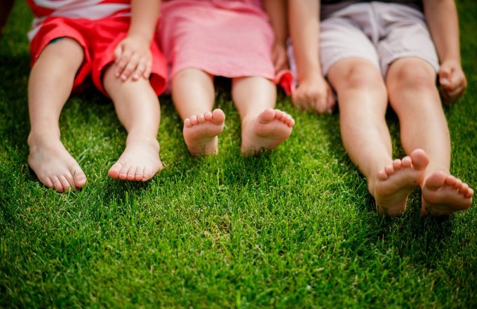 children's legs on the grass. bare legs of little girls sitting on the meadow. Selective focus, children sit on the grass with bare legs