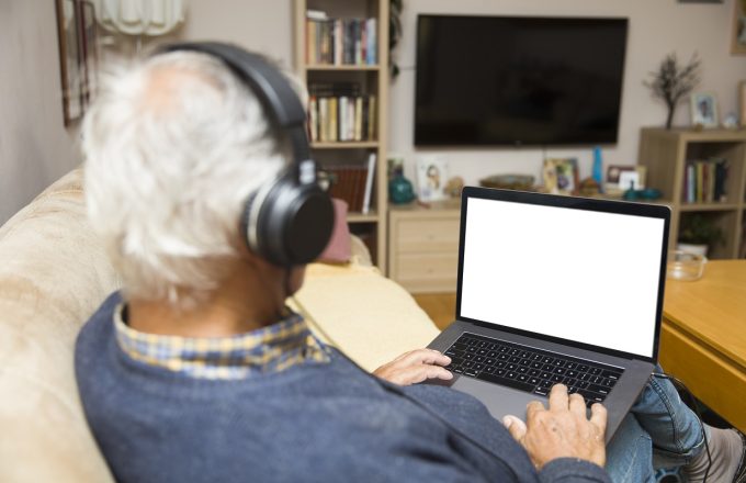 Modern elderly man siting at home with earphones and having online video call