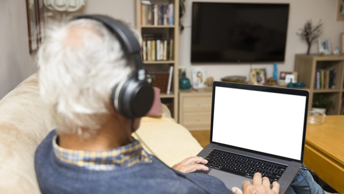 Modern elderly man siting at home with earphones and having online video call