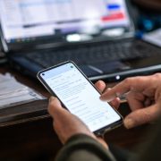 Image of a laptop in use in background and a mobile phone in use in the foreground