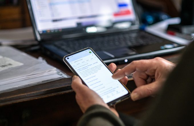 Image of a laptop in use in background and a mobile phone in use in the foreground