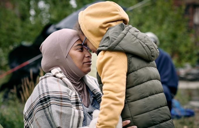 Happy middle-eastern mother in headscarf touching foreheads with daughter while finding her after escape from battlefield