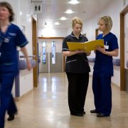 Nurses discuss information in a clipboard folder in a hospital corridor. Communication. Two women. Staff. Hospital environment.