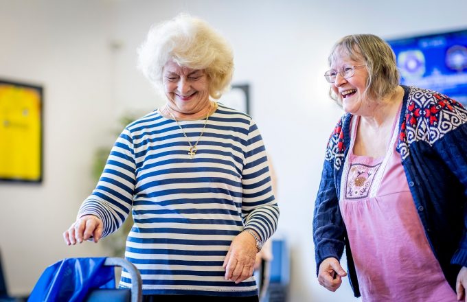 Two older women laugh together in a shared space