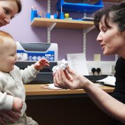 A doctor holds up a paper bird to a baby in a GP surgery
