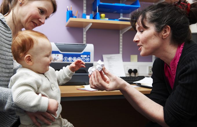 A doctor holds up a paper bird to a baby in a GP surgery