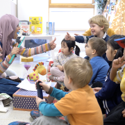 A stryteller sits on the floor to tell a story at a nursery surrounded by children