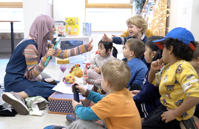 A stryteller sits on the floor to tell a story at a nursery surrounded by children