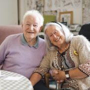 An older couple lean into each other smiling in a care home setting