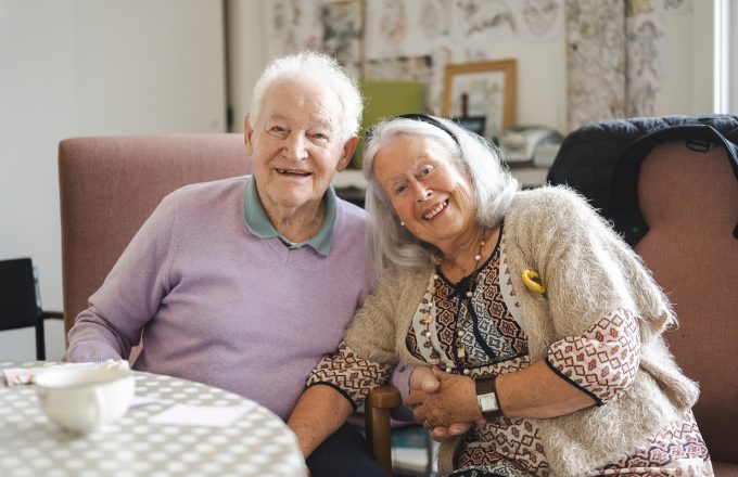 An older couple lean into each other smiling in a care home setting