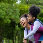 African American mother is playing piggyback riding with her young daughter in the public park