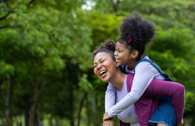 African American mother is playing piggyback riding with her young daughter in the public park