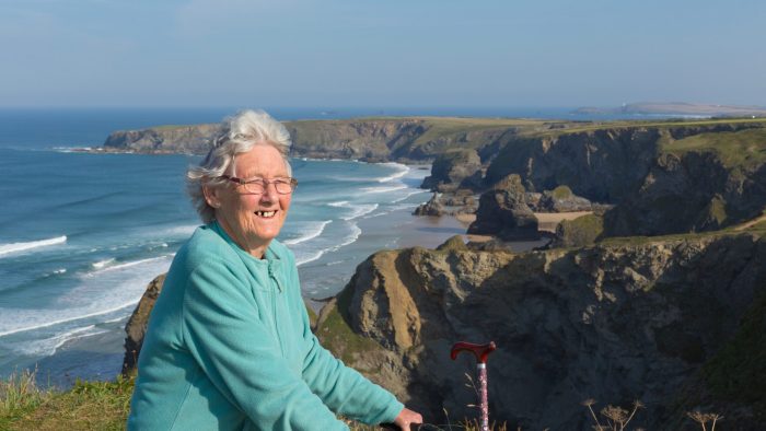 Happy elderly female pensioner by coast scene Cornwall England UK