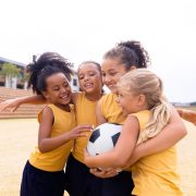 A group of girls hug while playing football