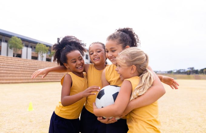 A group of girls hug while playing football