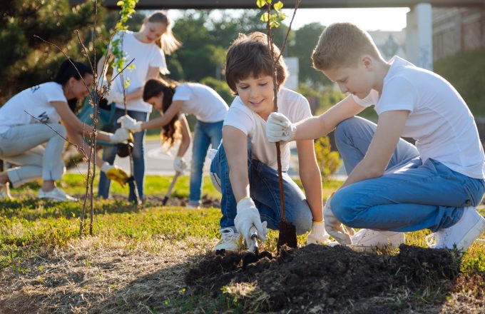 Kids planting trees and helping each other, smiling.