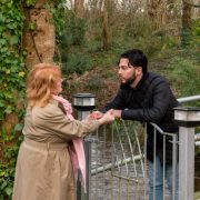 A man leans over a gate to hold the hand of a woman on the other side