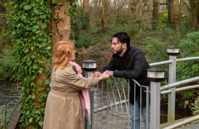 A man leans over a gate to hold the hand of a woman on the other side