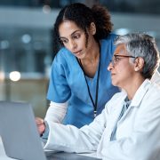 Two female clinicians look at a laptop together