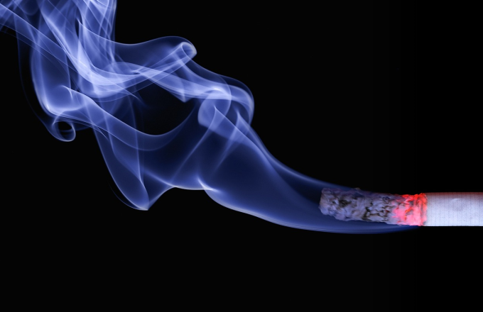 A lit cigarette over a black background with blue-white smoke billowing from the end.
