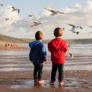 Two young children in warm clothes feed seagulls on the beach.