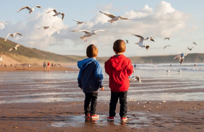 Two young children in warm clothes feed seagulls on the beach.