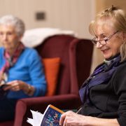 Two older women reading books and smiling in a care home setting.