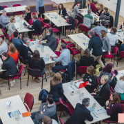 Aerial shot of a large group conference, backs of heads, facing a presentation out of shot.