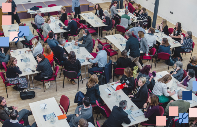 Aerial shot of a large group conference, backs of heads, facing a presentation out of shot.