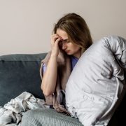 A young woman with long covid syndrome sits on a sofa, clutching her head.