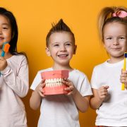Smiling children hold large toothbrushes and teeth up to the camera