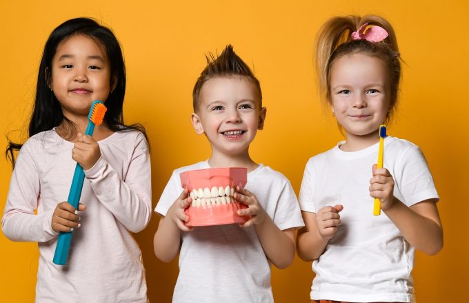 Smiling children hold large toothbrushes and teeth up to the camera