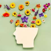 Paper face over pale green background, fresh flowers laid out over top of head representing mental health